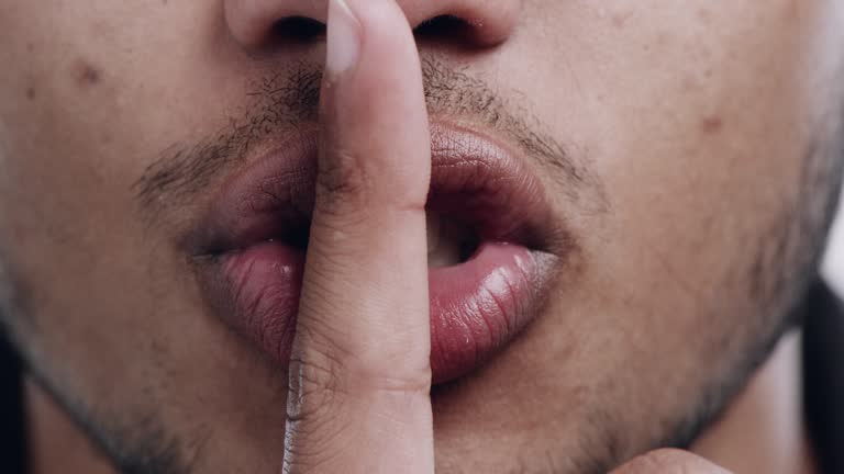 4k video footage of an unrecognizable man standing alone in the studio and putting a finger to his lips