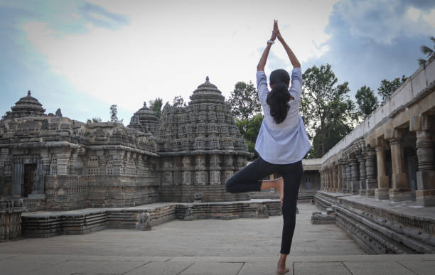 una ragazza indù in piedi su una gamba e le mani alzate sono in postura yoga nei locali del tempio durante le ore del crepuscolo a somanathapura, karnataka, india. - indian ethnicity traditional culture architecture karnataka foto e immagini stock