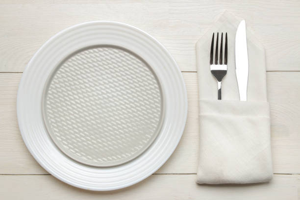 istock table setting. cutlery. Fork, knife in a napkin and a plate on a white wooden table. top view 1332659234