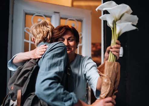 Senior woman greeting young man with bunch of flowers at the door