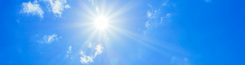Bright sun with beautiful beams in a blue sky with some light clouds. Space for copy.