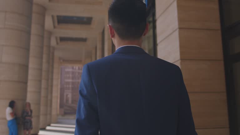 A successful young man in a business suit is walking down the street on a sunny day. The camera shoots the man from behind and moves behind him. His startup program for automating enterprise management processes was highly appreciated.