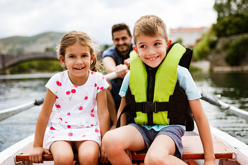 Young happy family enjoying boat ride on a river. Single father with his children enjoying vacation.