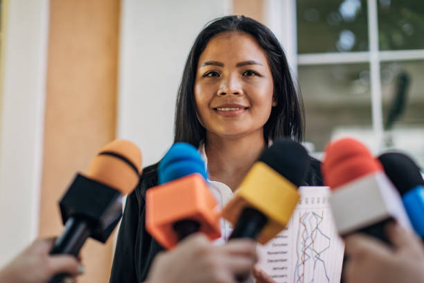 Asian politician speaking to reporters One woman, Asian female politician talking into reporters microphones. spokesperson stock pictures, royalty-free photos & images