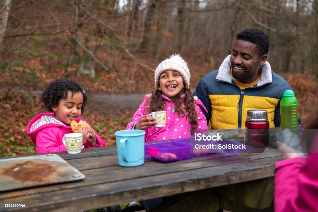 Enjoying Their Picnic A family sitting at a picnic table in Plessey Woods, Northumberland. They are eating and drinking while taking a break from walking and exploring the woods. Family Stock Photo