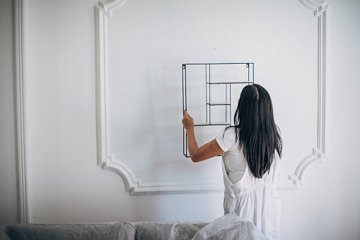 One woman, beautiful Asian female putting a shelf on the wall after painting in living room at home.
