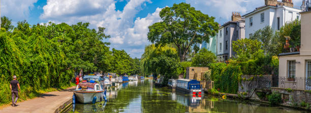London narrow boats along Regents Canal Camden Lock homes panorama People enjoying the summer sunshine along the tranquil waters of the Regent’s Canal outside Camden Lock in the heart of Central London, UK. regents canal stock pictures, royalty-free photos & images