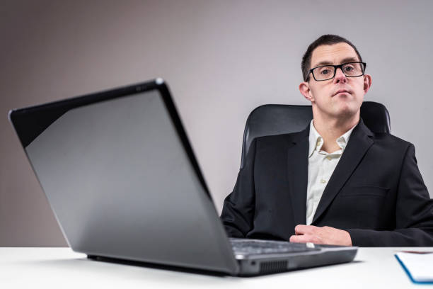 Down syndrome young businessman, sitting on his chair, laptop on his desk, looking professional and serious