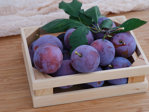 Freshly harvested blue plums with leaves in a wooden box. Close up.