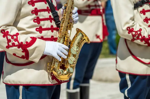 Photo of Golden saxophone. Stage, Shipka. A man is playing the saxophone. A musician from a military band plays the saxophone. Military parade uniform. A police band plays on Shipka Peak, Bulgaria.