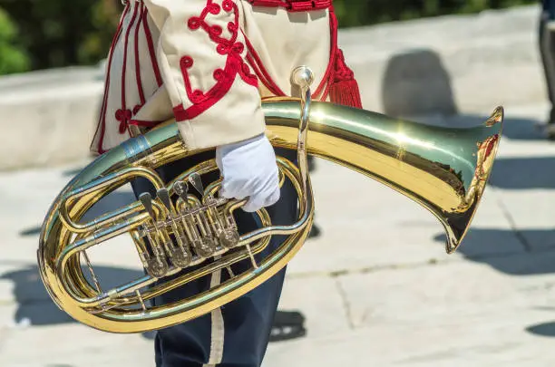 Photo of Golden tube. Scene, Shipka. A man is playing the tuba. A musician from a military band holds a tuba. Military parade uniform. A police band is playing on Shipka Peak, Bulgaria.