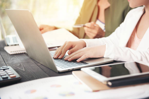 istock Side view of businesswoman's hands using laptop computer placed on messy office desktop. teamwork with business people analysis cost graph on desk at meeting room. 1332682557