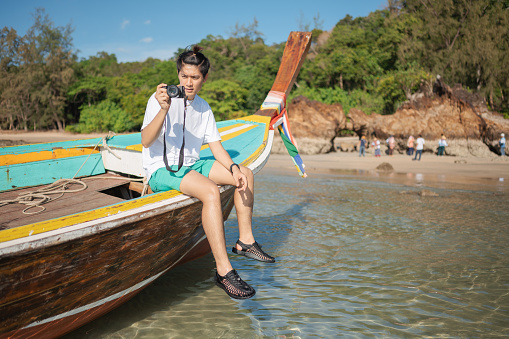 Traveling in Thailand. Asian toursit man sitting on the head of wooden longtail boat travel on the sea go to the amazing island and lagoon nature in vacation.Phi Phi Island