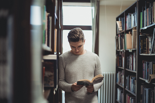 A young man, a young student in a library, is looking for literature.