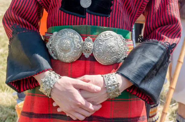 Vintage silver jewelry. Traditional women's clothing. A young woman in Bulgarian folk costume. Silver ornaments, red robe and silver belt. Women's hands up close. Bulgarian folklore. Female hands.