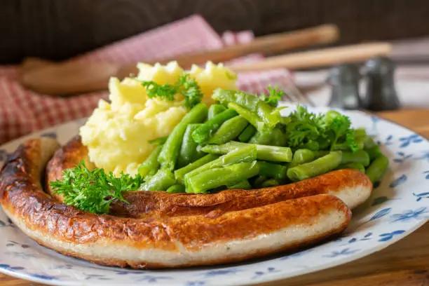 Traditional german meal with fried bratwurst served with mashed potatoes and green beans on a plate. Closeup and isolated view