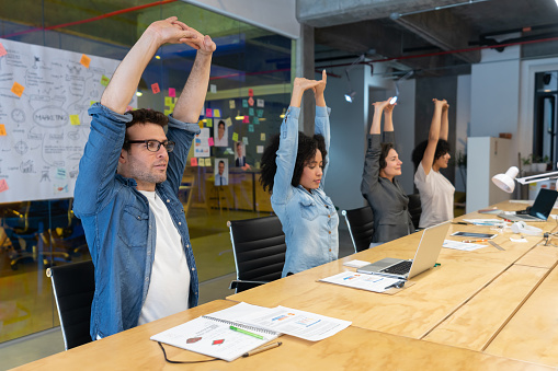 Trabajadores haciendo ejercicios de estiramiento en una reunión de negocios en la oficina photo