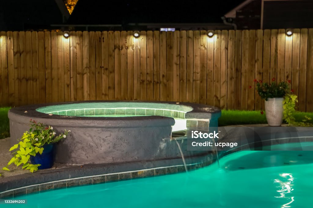 A backyard swimming pool and Hot Tub hot tob at night A backyard swimming pool and Hot Tub hot tob at night with solar lights around the fence for privacy and illumination. Hot Tub Stock Photo