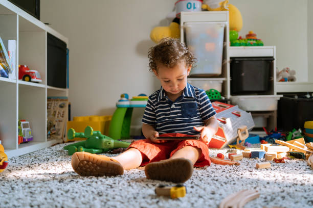 niño latino sosteniendo un teléfono celular en la sala de juegos - preschooler child playing latin american and hispanic ethnicity fotografías e imágenes de stock