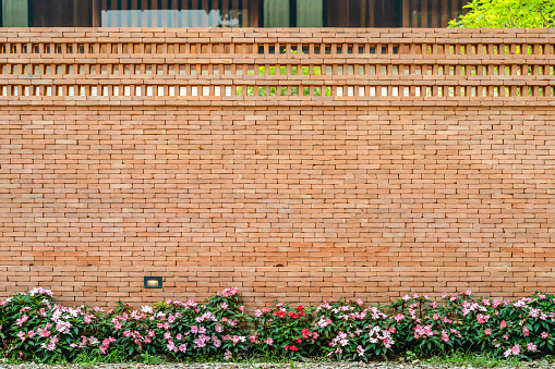 The backdrop of Brick wall with pink - white flower on the bottom for architecture and nature combination background story.