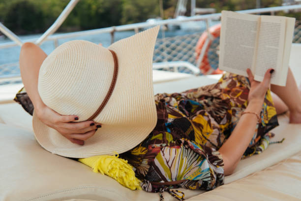 istock Woman with straw hat reading book at yatch, enjoying her vacation 1332701165