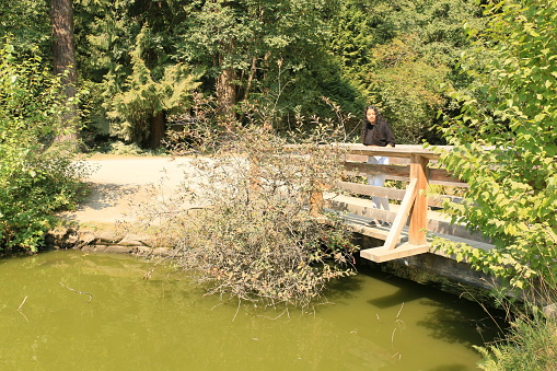 A woman on a bridge in a park. She has a black shirt on.