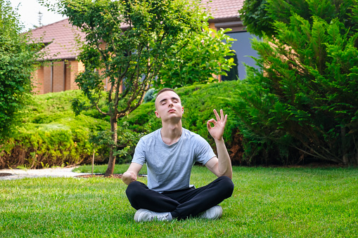 Young caucasian man with amputated arm meditating yoga in lotus pose outdoors in his backyard in summer