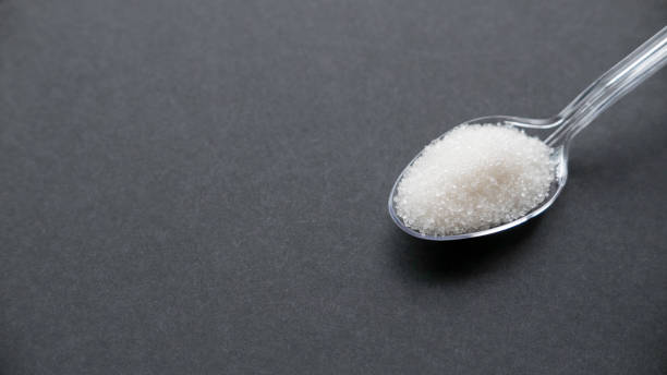 istock A white sugar in a transparent spoon on a black background with copy space. 1332706493