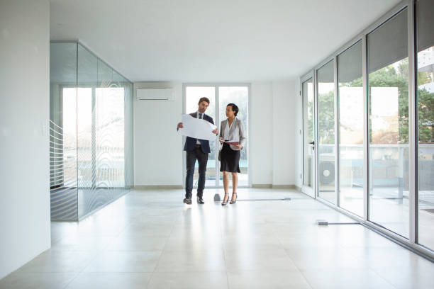 Latin female and male architects walking around in empty office while discussing over blueprint