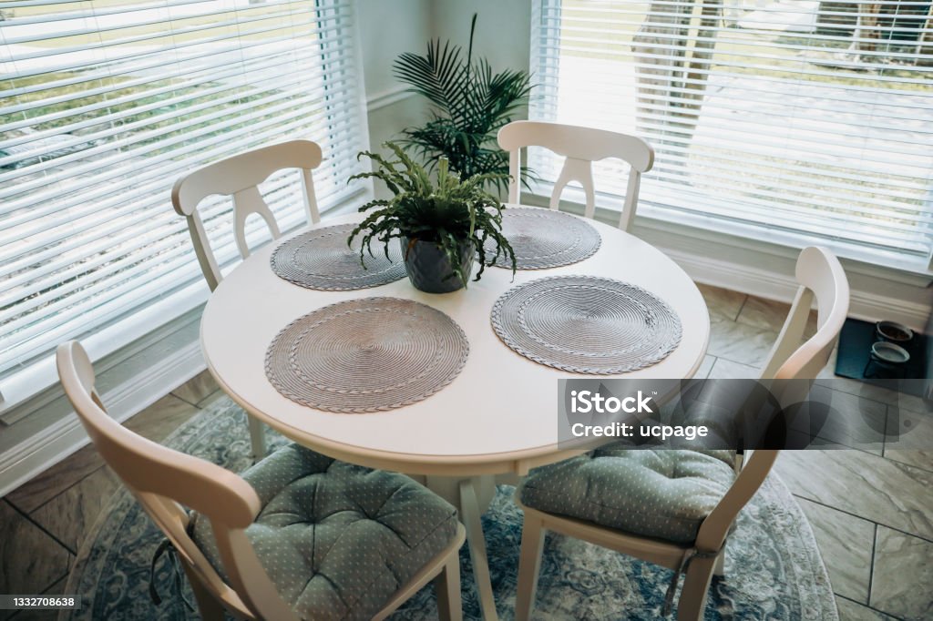 Close up of a small table and four chairs in an eat in kitchen with a tile floor Close up of a small table and four chairs in an eat in kitchen with a tile floor, a rug, plant, and placemats. Dining Table Stock Photo