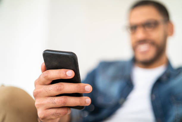 istock Cheerful mid adult man text messaging while sitting on sofa at home 1332708681