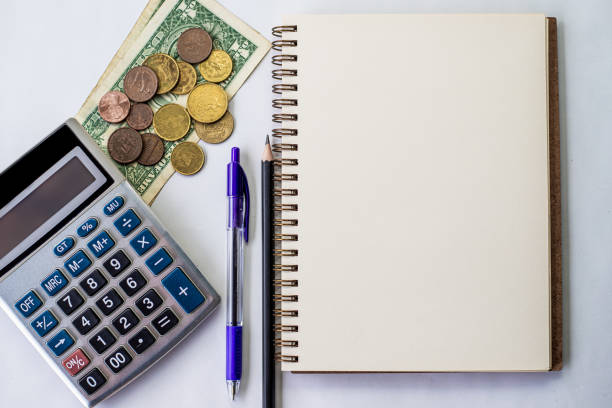 istock Plain Spiral Notebook With Pen Beside Calculator And Coins On Table. Simple Notepad And Ballpen Alongside Calculation Machine Placed On Top Of Desk. 1332712676
