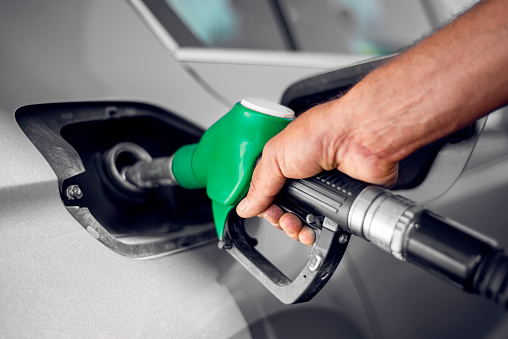 Un hombre sostiene la boquilla de combustible verde en el tanque de gasolina de un automóvil en la gasolinera photo