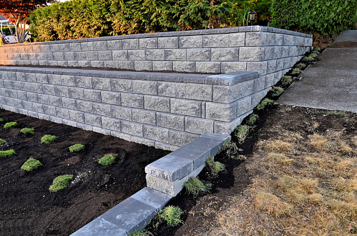 A side view of a staggered retaining wall build as a two tier wall in gray color a beautiful hardscape design completed in the front yard.