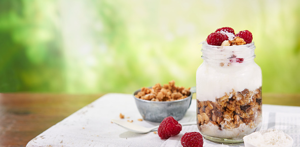 Granola with greek yogurt parfait fresh raspberries, coconut in a glass on wooden table outdoors. Healthy and tasty summer breakfast. Food Banner background with copy space.