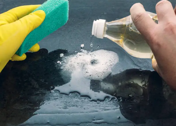 Caucasian man, with a green sponge in his hand and yellow gloves, adds vinegar to baking soda to clean a surface.