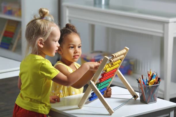 los niños de diferentes razas se sientan juntos en la mesa y cuentan con el ábaco - preschool fotografías e imágenes de stock