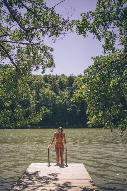 istock Young woman walks down dock ladder, into lake 1332729036