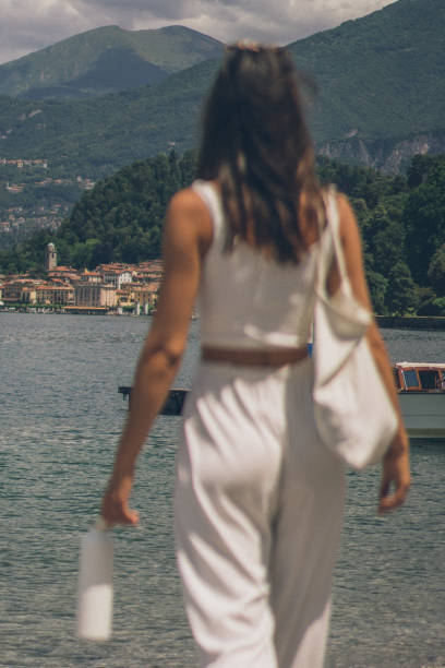 View of young woman walking down towards lake She looks off towards forested village in the distance crop top view stock pictures, royalty-free photos & images