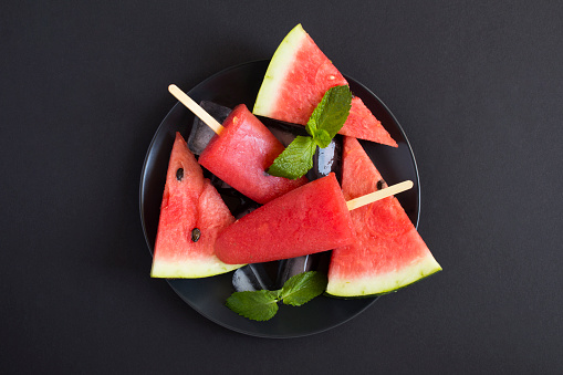 Top view of popsicles with watermelon on the black plate on the black background. Close-up. Copy space.