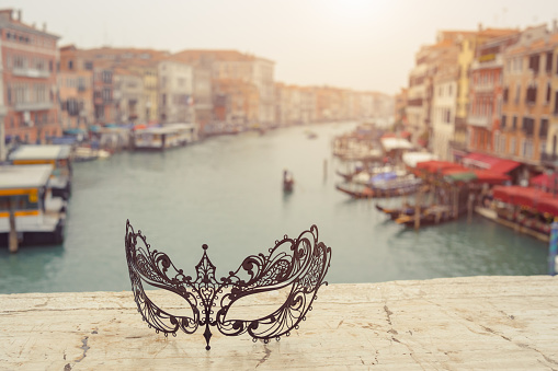 Venetian masks on bridge agaist beautiful landscape Grand Canal with gondolas and boats in Venice, Italy . Annual carnival in Venice is among the most famous in Europe. Venice is a popular tourist destination of Europe.