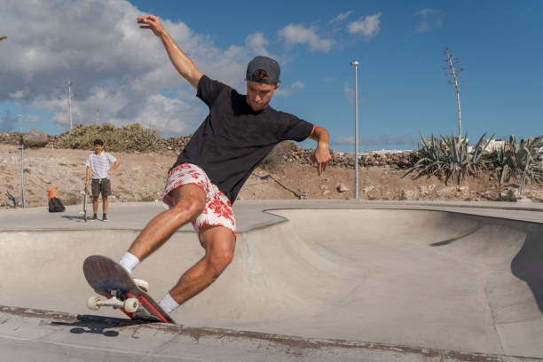 il giovane skateboarder fa un trucco chiamato "rock to fakie" ai margini di una piscina in uno skate park. vista frontale - fakie foto e immagini stock