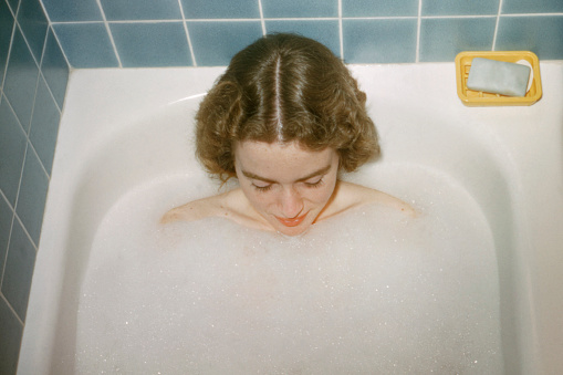 Young caucasian woman with strawberry blonde hair and freckles taking bubble bath from above Scanned film.