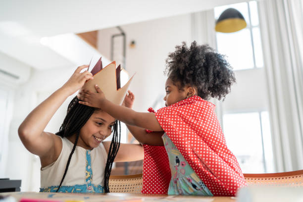 Sisters preparing costume, drawing and doing art and craft at home - wearing a paper crown and cape