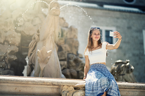 Teenage girl sightseeing the city of Salzburg. They are sitting by the Residence Fountain in Residenzplatz city square. \n\nShot with Canon R5