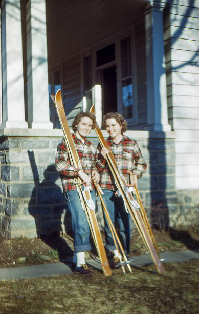two young women ready for ski trip 1950 Two young women, twins, posing in front of house with matching wooden skis and flannel shirts before ski trip. Springfield, Pennsylvania USA January 1950, scanned film. ski photos stock pictures, royalty-free photos & images