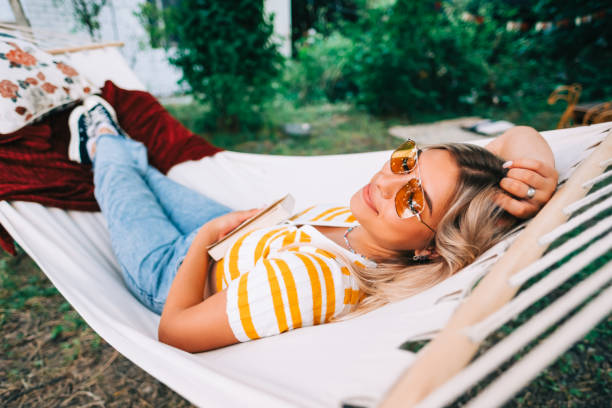 Young woman relaxing in hammock outdoors, in the backyard garden. Enjoying summer Young woman relaxing in hammock outdoors, in the backyard garden. Enjoying summer hammock relaxation women front or back yard stock pictures, royalty-free photos & images