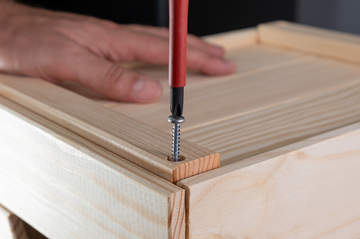 Assemble the wood product by turning the screw into a wooden plank with a manual screwdriver. Tightening. Easy assembly and DIY concept.