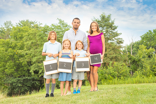 A family portrait with kids holding chalkboards with numbers on them and mom holding the fourth over her pregnant belly.