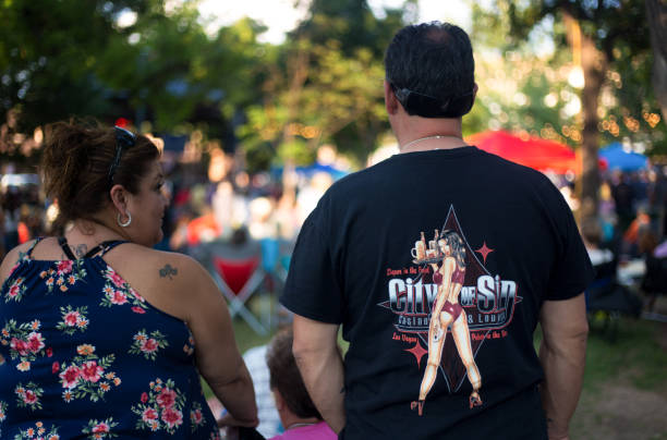 Santa Fe, NM: Tattoo and Sexy T-Shirt Couple on Plaza Santa Fe, NM: A middle-aged Latinx couple—one with a tattoo and another with a sexy T-shirt—standing on the historic Santa Fe Plaza. graphic t shirt stock pictures, royalty-free photos & images